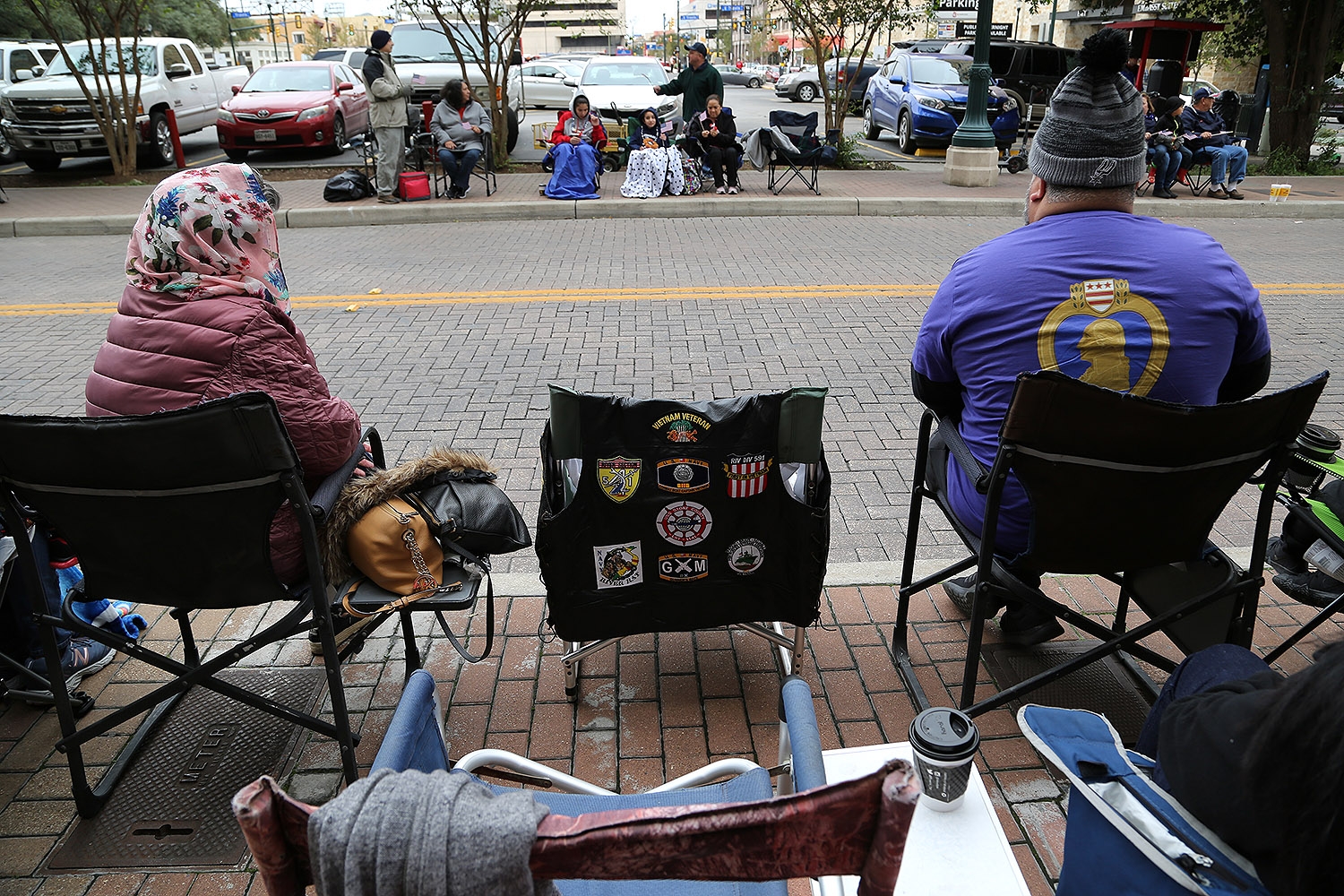 Sylvia Armendariz (left) sits next to a chair where her husband, Wenceslo, a Vietnam War veteran, would have sat. Wenceslo, who went by “Corky,” died on Memorial Day of this year. His family and friends came out to the Veterans Day Parade today to remember Corky and support other veterans. The Navy gunner’s mate received two Purple Hearts and the Bronze Star. He was 70. <em><b>Photo by Ben Olivo | Heron</b></em>